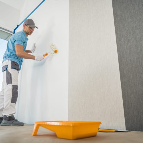 Caucasian Men in His 40s Applying Modern Canvas Textured Vinyl Wallpaper in the Apartment Room. Interior Renovation Theme.