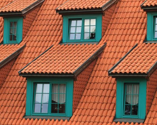 Close-up of an orange tiled roof with green framed dormer windows, creating a colorful architectural contrast.