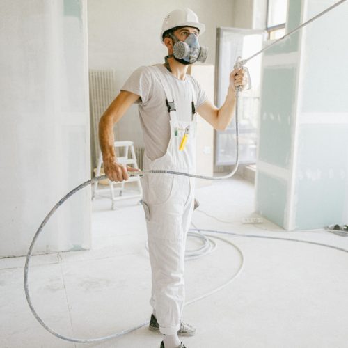 A construction worker in a white uniform using spray equipment inside a renovation site.